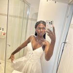 Stylish Afro-Latin American girl Conymegan taking a mirror selfie in a white dress inside a modern bathroom